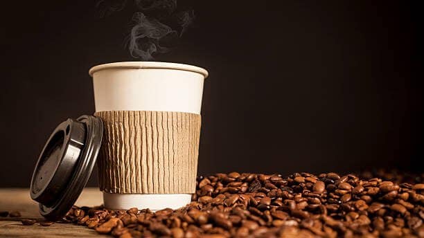 Teaming cup of coffee resting on a table covered with roasted coffee beans.